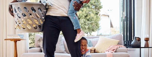 Parent and young child surrounded by laundry at home, capturing how kids transform laundry from a manageable chore into a constant, high-stakes demand