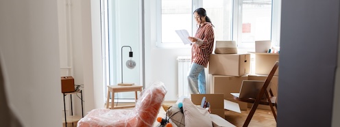 Person standing among moving boxes in a new apartment, representing the moment when laundry access becomes something that requires an actual plan for the first time