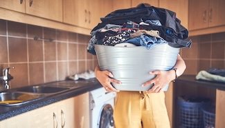 Person carrying an overflowing laundry basket, representing the hidden effort and time that goes into laundry beyond just running the machine