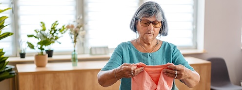 Older woman folding laundry at home, representing someone who has managed her household for decades now weighing whether to handle this task differently