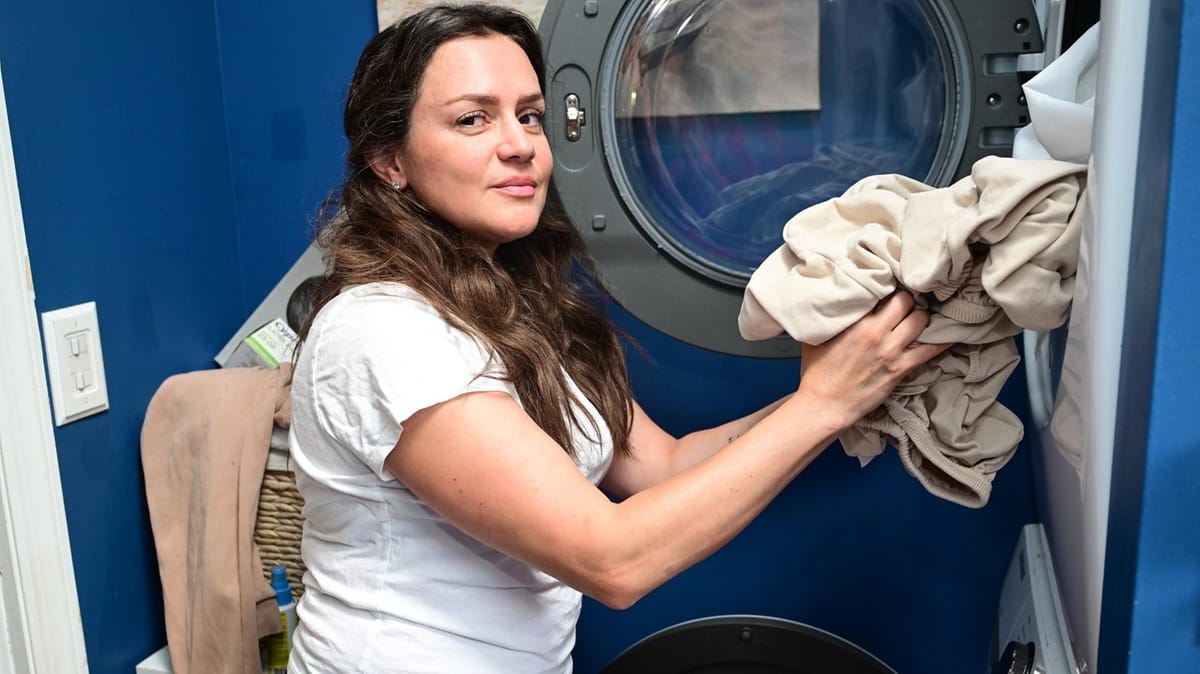 A woman loading laundry into a front-loading washing machine in her home laundry room.