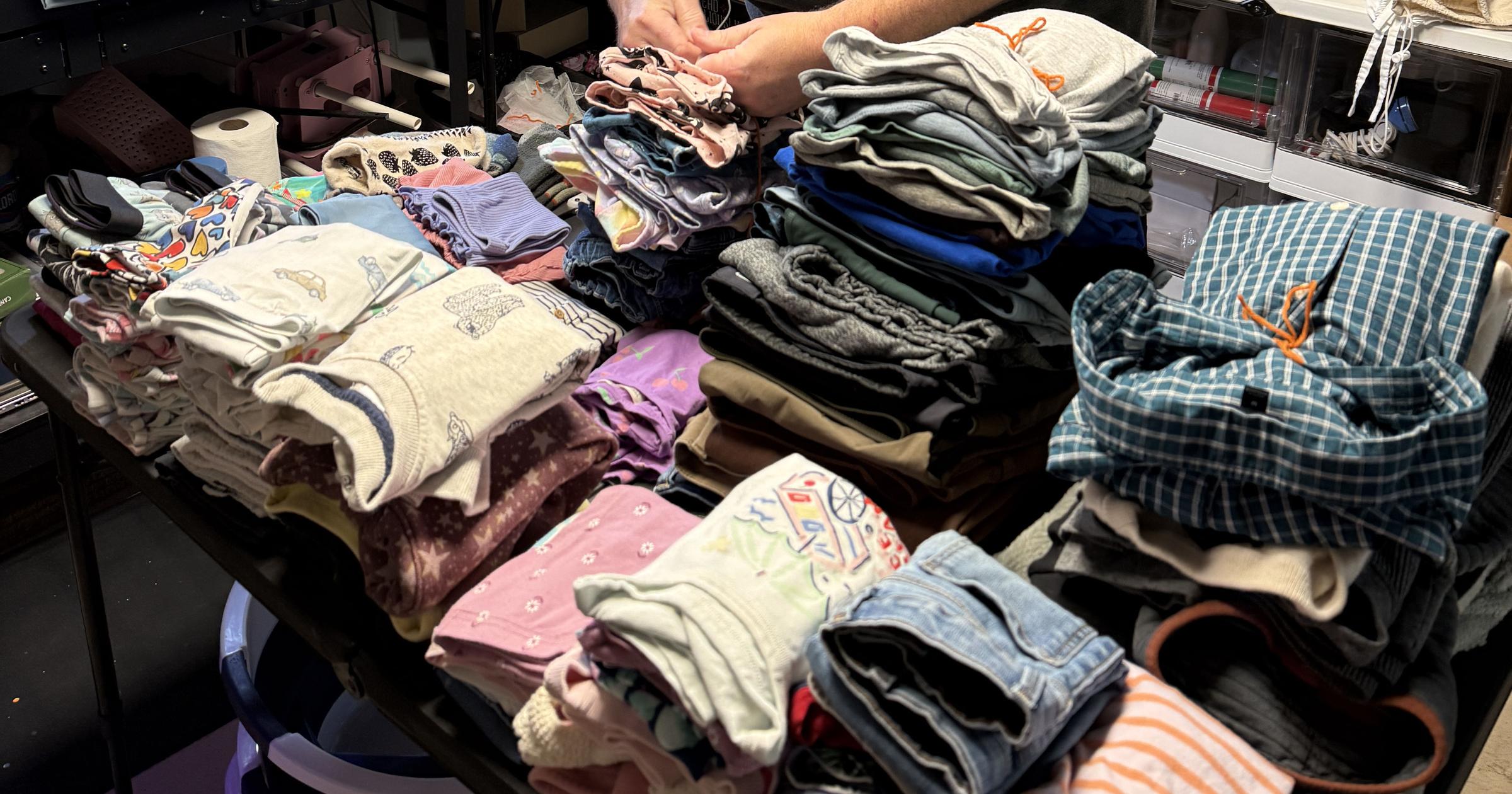 Hands folding laundry on a table piled with clothes.