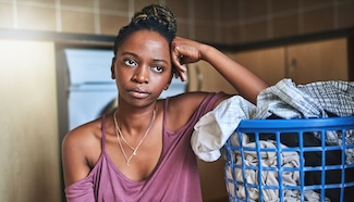 Woman sitting beside a laundry basket with a tired, resigned expression, capturing the feeling of another weekend claimed by laundry