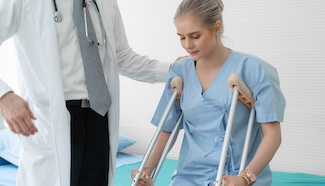 Woman receiving mobility guidance from a medical professional in a hospital setting, representing the recovery period during which laundry restrictions are in place and household tasks still need handling