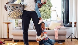 Parent and young child surrounded by laundry at home, capturing how kids transform laundry from a manageable chore into a constant, high-stakes demand