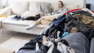 Pile of unfolded laundry in the foreground while a person rests in the background, illustrating how undone laundry lingers even when you're trying to take a break