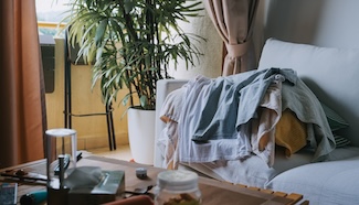 Pile of laundry on a couch in an apartment with warm interior lighting in the background, representing the weekly logistics problem of living without in-unit machines