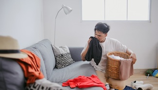 Person standing in a laundry room holding a basket surrounded by piles of clothes, conveying the exhaustion of trying to keep up when the demands have grown too large