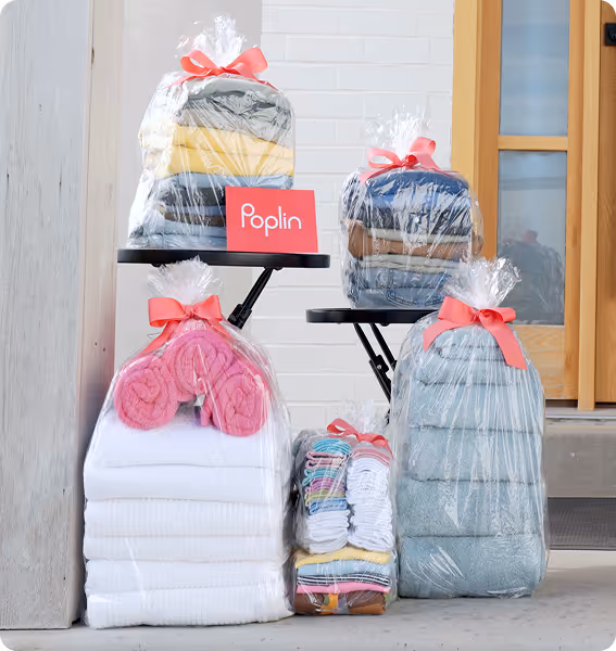 Stacks of folded laundry in clear bags with pink bows and a Poplin card, arranged by a front door.