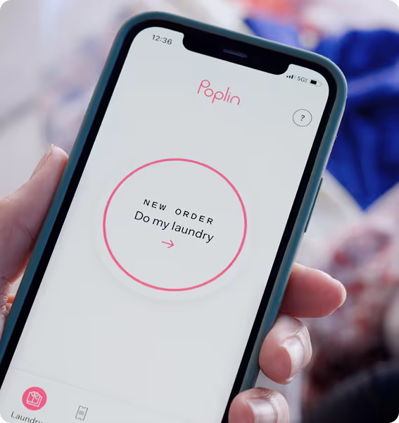 Hand holding phone showing Poplin app screen with a button labeled “New Order: Do my laundry.
